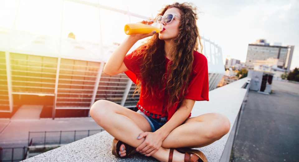 young hipster woman with curly hair sunglasses drinking fresh orange juice from bottle